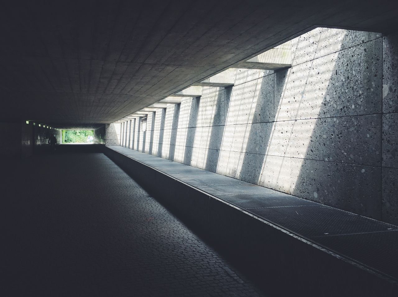 Architectural view of a concrete tunnel featuring striking sunlight patterns on the wall.