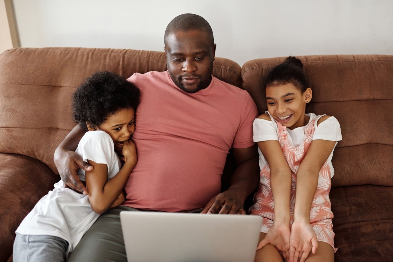 Happy father cuddling with children on sofa while watching something fun on a laptop indoors.